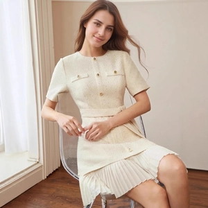 Detail of cream tweed dress featuring gold buttons and white pleated hemline detail