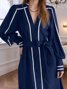 Detail eines eleganten dunkelblauen V-Ausschnitt-Kleids mit weißer Paspelierung