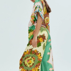 Detail of vibrant fruit print and green polka dot border on silk-texture resort set