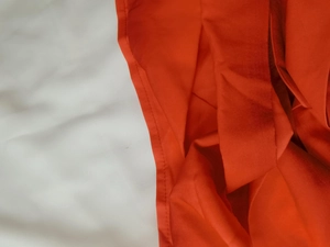 Detailed view of bright orange-red fabric with refined pleated texture and sewing lines