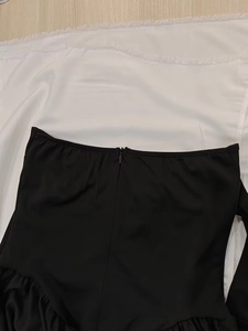 Detail of solid black high waist dress featuring invisible back zipper and ruffled hemline