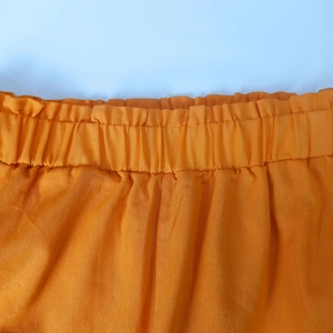 Detail view of the elastic waistband with ruffled edges on casual orange pants