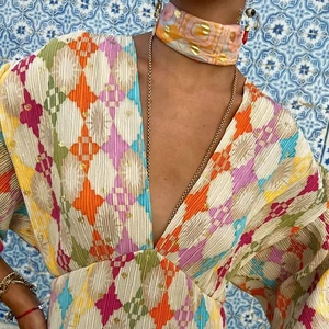 Detail of V-neck pleated dress with colorful geometric print and gold foil accents