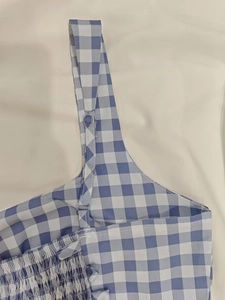 Détail des bretelles réglables et du tissu smocké à carreaux vichy bleu sur la robe