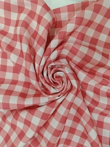 Gros plan du tissu vichy rose et blanc montrant la texture douce et un pliage en spirale