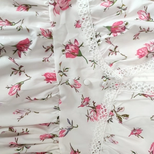 Close-up of white floral dress with pink rose print, lace trim and button detail