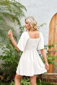 Close-up of white mini dress featuring textured fabric and back elastic smocking detail
