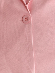 Détail d'un blazer rose à col en V montrant les boutons en résine et la texture du sergé