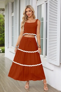 Dettaglio di crop top senza maniche rosso ruggine e gonna maxi con bordo ric-rac bianco