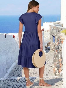 Detail view of tiered hem and ruffled sleeves on a navy blue midi dress in a resort setting