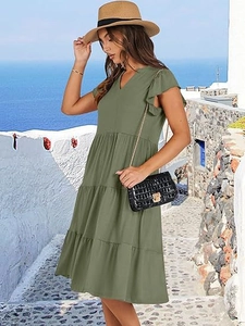 Detail of green V-neck dress with ruffle sleeves and tiered skirt in a seaside setting