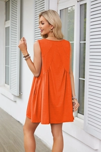 Detail of orange sleeveless dress showing back geometric seams and pleated A-line hem fabric
