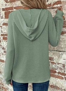 Detailed back view of waffle knit hoodie in sage green against a rustic brick wall