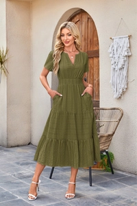 Detail of olive green V-neck dress featuring tiered skirt and textured fabric in outdoor garden