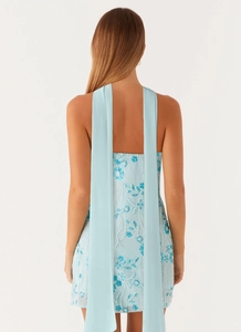 Close-up of light blue sequined mini dress featuring floral beadwork and long back ribbons