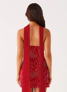 Detailed view of red sequin mini dress featuring intricate beadwork and hanging back ribbons