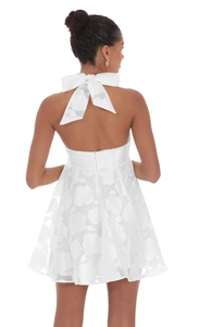 Close-up of white backless dress featuring 3D floral texture and a large neck bow tie