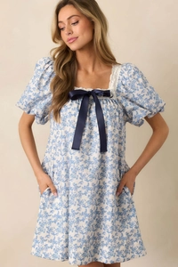Detail of blue floral dress with lace square neck and decorative navy bow on chest