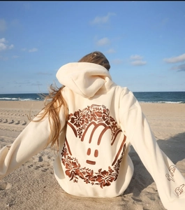 Close-up of brown floral embroidery on a beige drop-shoulder hoodie back in a beach setting