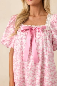 Close-up of pink floral dress featuring white lace square neck and large satin bow