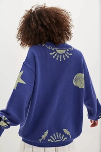 Detail showing dark blue knit sweater with yellow ocean sun and seashell embroidery
