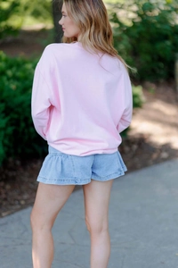 Détail d'un sweat-shirt rose associé à un short en jean à volants bleu clair au jardin