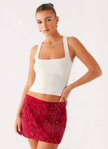Nahaufnahme von weißem Strickoberteil und rotem Minirock mit floralen Pailletten