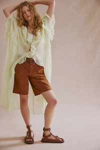 Detail of light green ruffled chiffon cardigan with brown suede shorts and studded sandals