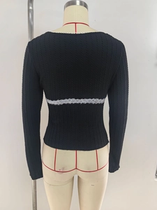 Detail of black knit top with cable texture and white lace trim on the back waistline