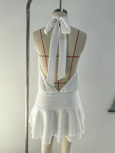 Detail view of white crochet halter dress featuring an oversized back bow and tiered hem
