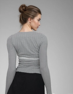 Detail of grey cable-knit top featuring delicate white lace trim on waist and back
