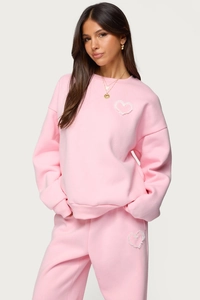 Detail of pink two-piece tracksuit featuring white lace heart patches and cotton blend fabric