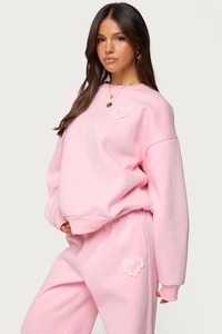 Detailed close-up of pink hoodie set featuring white lace heart patches and cotton texture