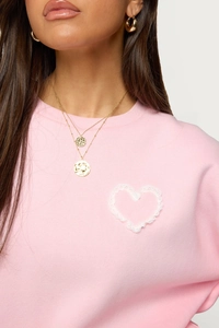 Close-up of pink hoodie with white lace heart detail and gold layered necklace