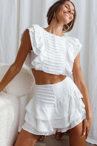 Detail of white two-piece set featuring flutter sleeves and delicate ruffle pom-pom lace trim