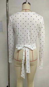 Detail view of the back tie-knot bow design on this white polka dot long sleeve top