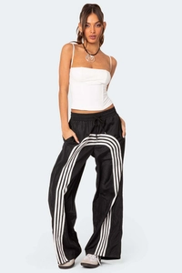 Fotomodel in weißem, engem Crop-Top und schwarzer, weiter Sporthose mit markanten Seitenstreifen