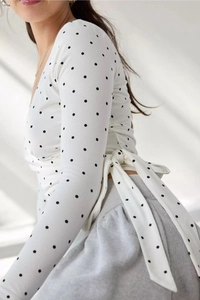 Detail of white polka dot wrap top featuring a waist tie and soft knitted fabric