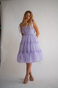 Detail eines hellvioletten ärmellosen Kleides mit Schleifenträgern und Rüschensaum