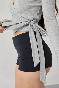 Detail of grey wrap-around long sleeve top with waist tie and black high waist shorts