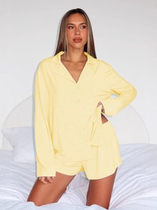 Women's pale yellow long-sleeve pajama set with button-down shirt and shorts in a bedroom