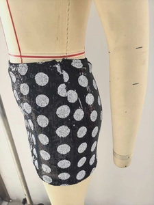 Detail view of the hidden side zipper on a black sequined mini skirt with white polka dots