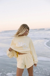 Primer plano de conjunto informal amarillo claro con sudadera NCY y pantalón corto en playa