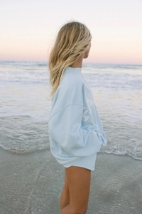 Detalle de sudadera oversize azul claro con letras EA blancas en el atardecer costero
