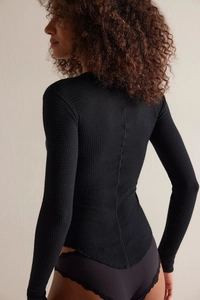 Detail of waffle-knit black bodysuit featuring delicate lace trim and fitted sleeves