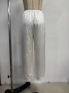 Detail view of white satin pajama pants featuring delicate lace trim at the hemline