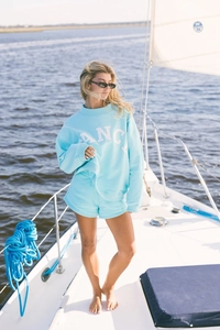 Detalle del conjunto de sudadera azul claro con logo FANC en un fondo de velero soleado