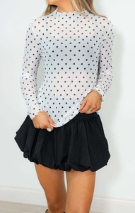 Detail of white sheer mesh top with black polka dots and delicate ruffle neckline