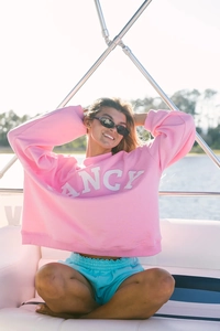 Detalle de sudadera rosa con bordado FANCY y pantalones cortos azules en la cubierta de yate