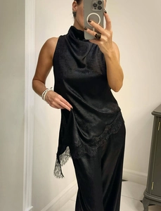 Macro shot of asymmetric black satin top with delicate lace trim and mock neck detail